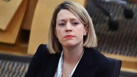 Getty Images Education Secretary Jenny Gilruth, who has a blonde bob, red lipstick and a black blazer, sitting in the Holyrood chamber