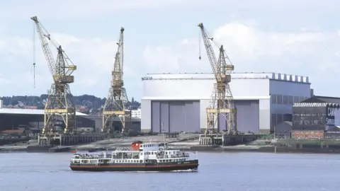 A ferry on the River Mersey with cranes in the background