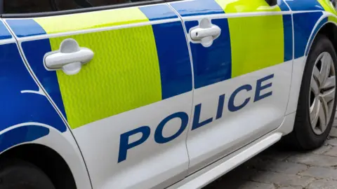 Close-up picture of a United Kingdom police patrol response car with Battenberg markings and the word police in capital blue letters.