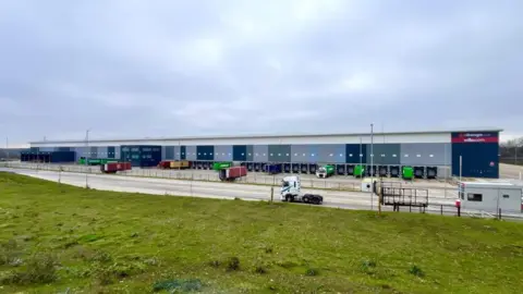 Martin Giles/BBC There is a large warehouse structure with various containers in bays located outside. It has the Range and Wilko written on the side.