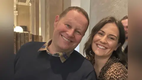 Jason is a bald man with blue eyes and he is smiling next to his daughter Abbey, who has long dark hair and is also smiling.