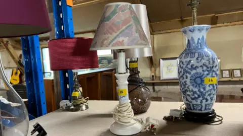 Five lamps with shades standing on a desk. They each have yellow discount stickers on ranging from five to six pounds.