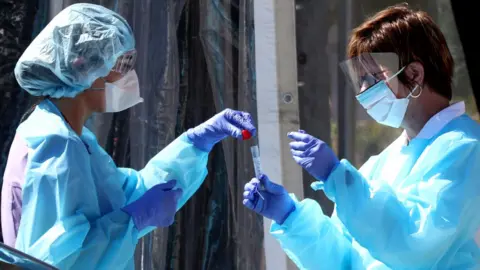 Getty Images Medical personnel secure a sample from a person at a drive-thru Coronavirus testing station in the US. 12 March 2020