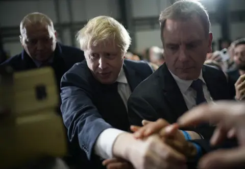 Christopher Furlong / Getty Images Boris Johnson shakes hands with supporters after a speech at a factory on December 10