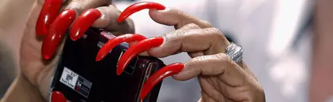 Getty Images Woman with long fingernails holds a camera