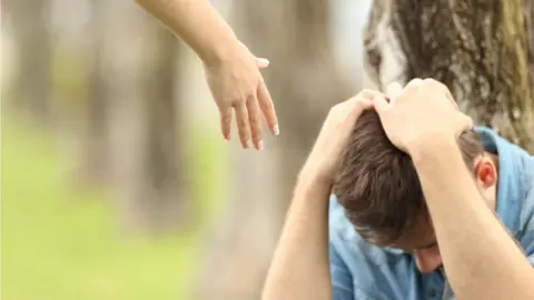 Getty Images A hand reaches down to a teenager sitting with his head in his hands