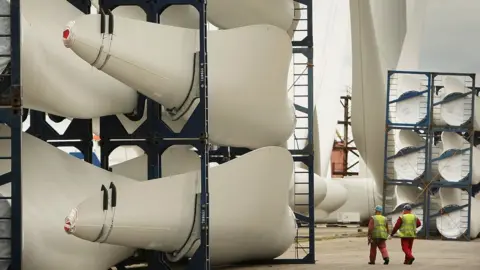 Getty Images Workers pass stored wind turbine blades at the Harland & Wolff shipyard