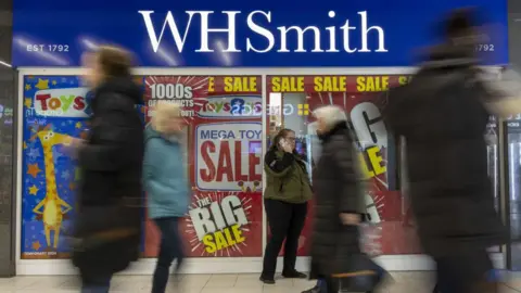 Getty Images Blurred people walking past a WH Smith high street store which has large sale signs in the window