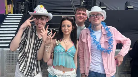 From left, Lennon, Jess, Ryan and Sam smile into the camera as they stand in front of one of the event's stages. They are dressed up with two of the boys wearing cowboy hats.
