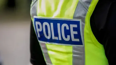 The back of a police officer wearing a high-vis vest with "police" in capital letters written on it