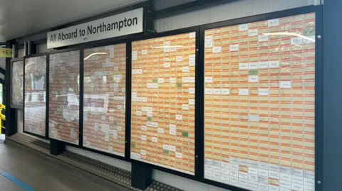 Kate Bradbrook/BBC The wall of orange rail tickets with white spaces left for the missing departure points