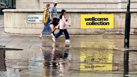 Simon Lamrock A large pool of water can be seen on the Euston Road, as people walk along the pavement 