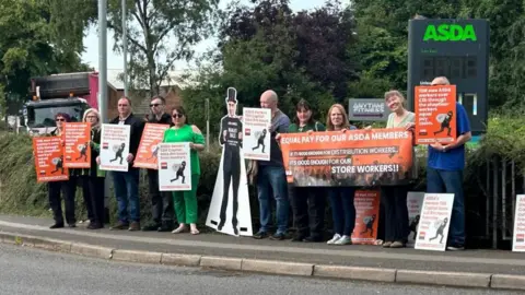 A line of 10 staff holding orange and white placards and a life-size cut-out of a figure in a top hat