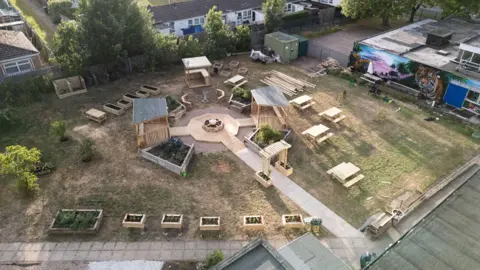 A drone shot of the finished garden from above. It shows wooden planters and benches on a grass space.