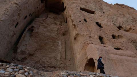 A file photo from March 2024 of a Taliban soldier standing guard in front of the ruins of a 1,500-year-old Buddha statue in Bamyan