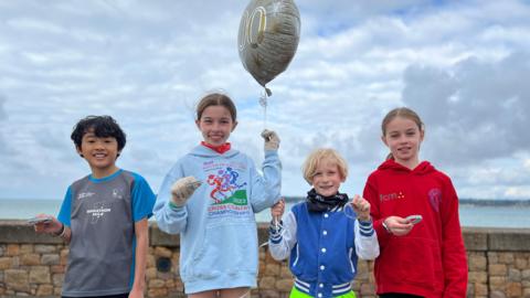 Sebastian, Florence, Xander and Zara are smiling at the camera holding their silver wristbands which celebrates their 100th junior Parkrun