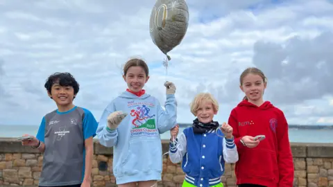 BBC Sebastian, Florence, Xander and Zara are smiling at the camera holding their silver wristbands which celebrates their 100th junior Parkrun