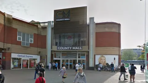 Google A Google Street image of the outside of the County Mall in Crawley. You see a number of people walking outside the entrance which has a sign which says "COUNTY MALL" above the sliding doors. At the top there is a large "CM" with "COUNTY MALL" below it.