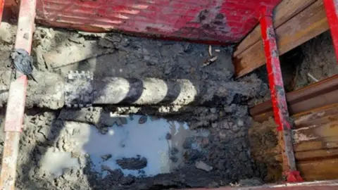 Thames Water Water pipe in muddy hole with wooden walls holding earth back in place.
