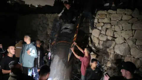 Getty Images Palestinians inspect debris of a missile fired from Iran to Israel, after it falls on an area in Luza neighborhood, Hebron Governorate in West Bank on October 1, 2024. 