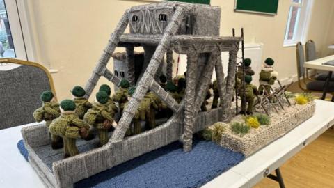 22 knitted soldiers holding rifles cross the knitted Pegas