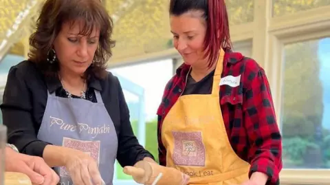 Surinder Hothi is showing another woman something just out of shot. They are both looking down onto a work surface.