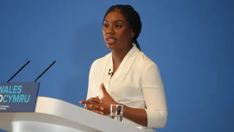 Kemi Badenoch speaking at Welsh Conservative conference in Llangollen, in front of a podium that says #FIXWALES in Welsh and English.