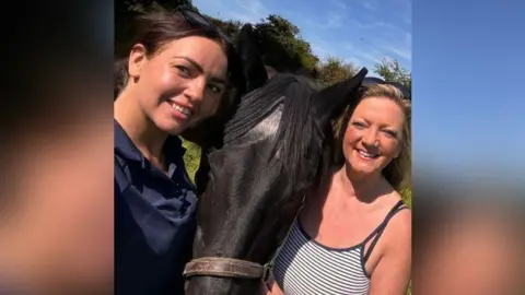 A selfie with Charlotte Walsh smiling on the left with her brown hair up in a ponytail, the horse Thorne in the middle and Sammy Boyle with her blonde hair down wearing a stripey vest and smiling on the right