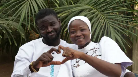 Olanrewaju and Kaosara next to each other using their hands to form a shape of a heart