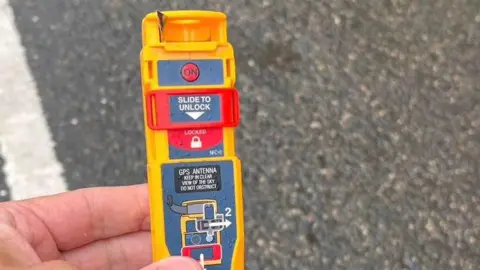 Jersey RNLI A hand is holding an  emergency position indicating radio beacon. The device is yellow, red and grey.