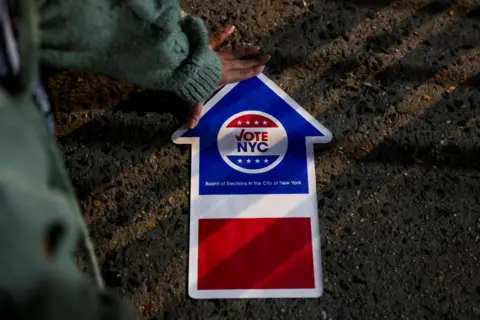 Andrew Kelly/Reuters A person gestures next to an election sign, on Election Day for the US presidential election in Manhattan, New York City, 5 November 2024 