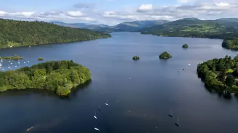 Reuters An aerial view of a large lake with numerous boats floating on it. It is surrounded by green hills and trees.