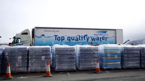 PA Media Pallets of bottled water in front of a South West Water lorry that says "top quality water"