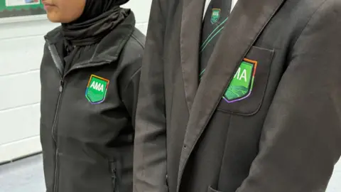 Two pupils stood side by side, one wearing the traditional blazer and tie uniform, the other, the new jacket and polo shirt