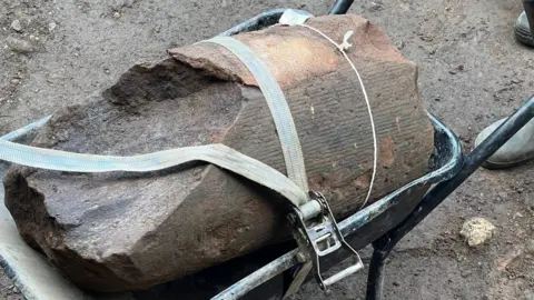 Uncovering Roman Carlisle A section of column found during an archaeological dig at Carlisle Cricket Club. The close-up image shows the column inside a wheelbarrow, secured with a security belt