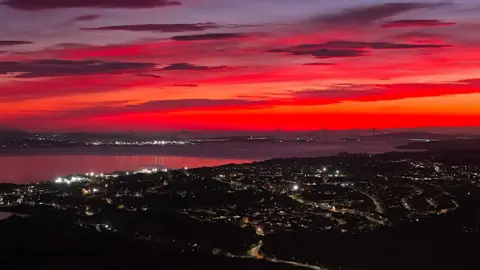 KEVIN HAMILL Brilliant shades of red and orange in the sky above West Lothian and Edinburgh in a picture taken at sunrise from atop a hill with the lights of the town of Bo'ness in the foreground. The outline of the bridges over the Firth of Forth can also be made out. 