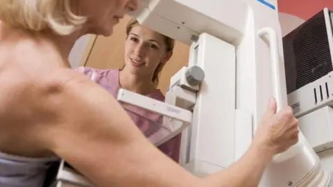 Getty Images A woman having a cancer screening with a nurse in the background