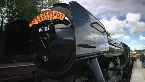 BBC The front on view of Flying Scotsman. It is black and has the words 'fox & edwards events' on the front of it.