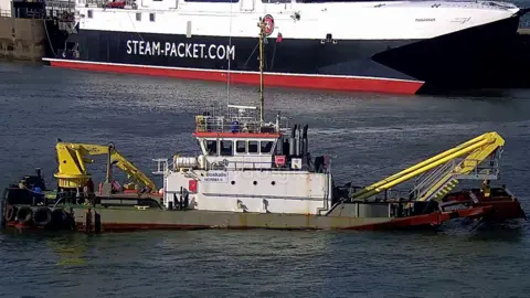 A dredging vessel in front of the Manannan fast craft ferry in Douglas Harbour.