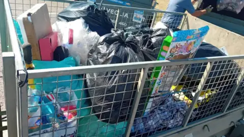 Thetford Town FC A metal trailer full of rubbish, including black waste bags, cardboard boxes and food packages.