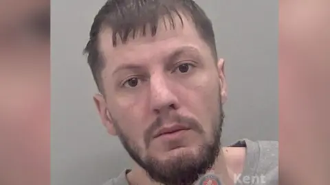 A police custody image of a man with a beard 