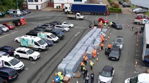 PA Media An aerial view of a carpark where stacks of bottled water are being collected by people and taken to their vehicles.