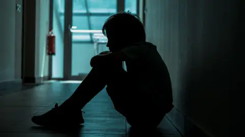 A child sitting in a dark corridor with his head on his knees.