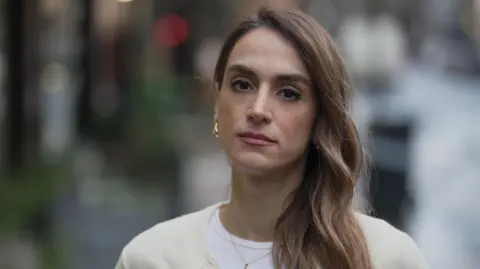 Mahsa Alimardani, a woman with long hair over her shoulder, stands in a street 