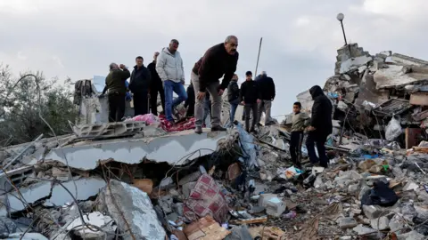 Reuters Palestinian inspect a building in Burqin, destroyed during an operation in which Israeli security forces killed two Palestinian men accused of killing three Israelis in an attack in the occupied West Bank (23 January 2025)