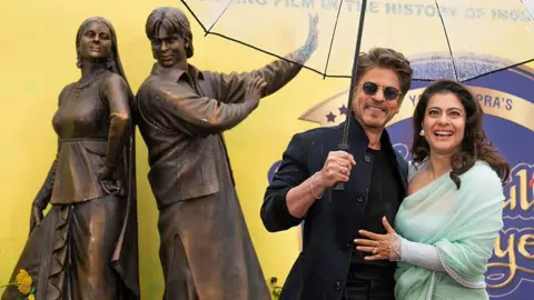 Getty Images Shah Rukh Khan and Kajol Devgan pose as a new bronze statue of Shah Rukh Khan and Kajol is unveiled at the Diwali Dulhania Le Jayenge 'Scenes In The Square' statue launch in Leicester Square on December 04, 2025 in London, England.
