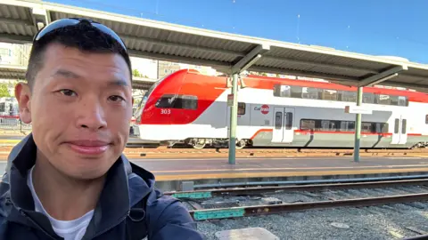 A selfie of William Hui in front of a public transit train