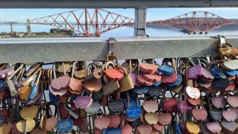 George Carson Coloured love padlocks with inscriptions are attached to the road bridge between South Queensferry and North Queensferry. The Forth Rail Bridge and the Firth of Forth can be seen in the distance. 