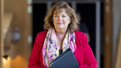 fiona hyslop wearing a red jacket walking holding a folder