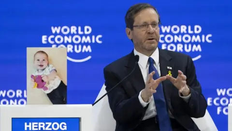 EPA Israeli President Isaac Herzog speaks next to a photograph of infant Israeli hostage Kfir Bibas, at the World Economic Forum in Davos (18 January 2024)